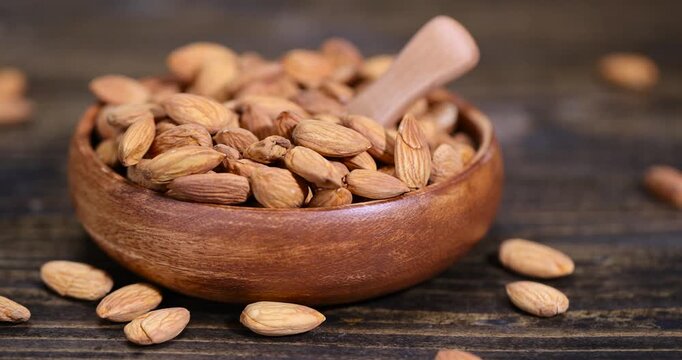 brown whole nuts of unroasted almonds with a wooden spoon on the table, a large number of hard raw almonds on the table during cooking