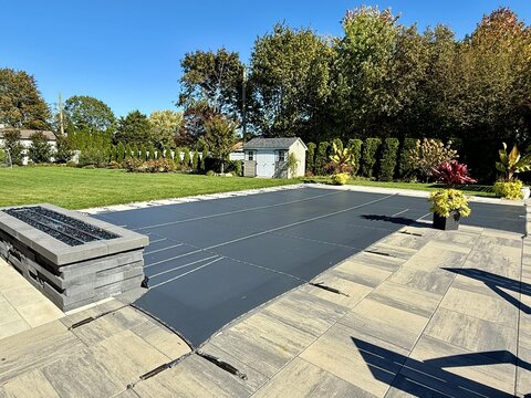 ready for winter in fall. custom winterized j-shaped built-in, inground pool with safety loop - loc mesh cover to protect. melting snow, rain drains through. brass anchors are flush to paver height.
