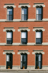 Brick building with multiple windows and flower pots in a city street during the day
