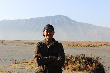 Confident Asian Young Man Traveler Posing with Arms Crossed in Volcanic Landscape. Represents confidence, exploration, and a successful journey.