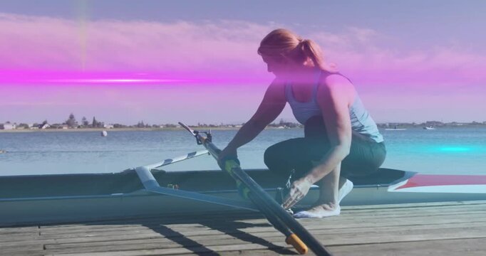 Stepping onto wooden dock, mature rowing athlete kneeling and adjusting oar rigging for boat launch