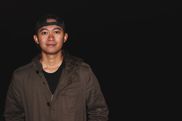 Young Asian Man Wearing Cap Portrait Against Dark Background with Copy Space. Studio-style portrait concept representing confidence, simplicity, and casual fashion for lifestyle or profile use.