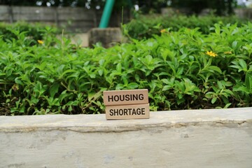 Two wooden blocks stacked to read HOUSING and SHORTAGE sit on a warm surface with lush green...