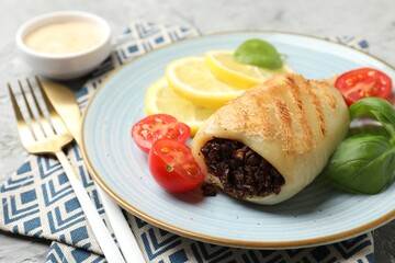 Piece of tasty grilled squid stuffed with mushrooms, basil, tomatoes and lemon on grey textured table, closeup