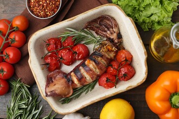 Tasty stuffed squid, rosemary and tomatoes in baking dish among other products on wooden table, flat lay