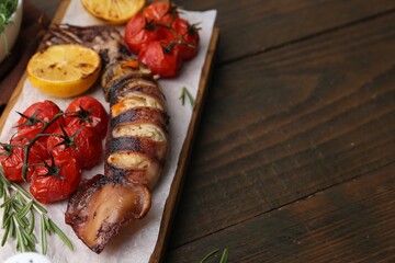 Tasty stuffed squid, rosemary, lemon and tomatoes on wooden table, closeup. Space for text