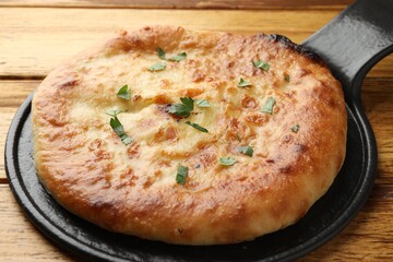Delicious Megrelian khachapuri with parsley on wooden table, closeup