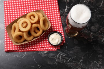 Fried squid rings with sauce and beer served on black marble table, flat lay