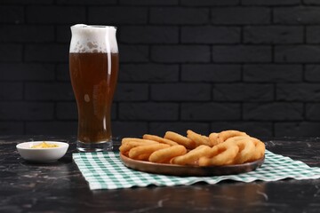 Fried squid rings with sauce and beer served on black marble table. Space for text