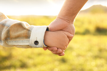Father holding hands with his son outdoors, closeup. Family bonding