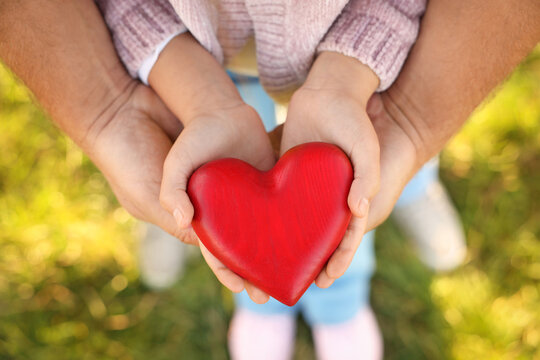 Father with his daughter holding red wooden heart together outdoors, closeup. Family bonding