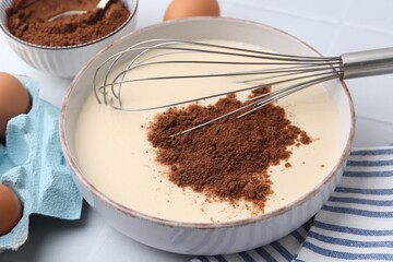 Adding cocoa powder into bowl with dough at white table, closeup