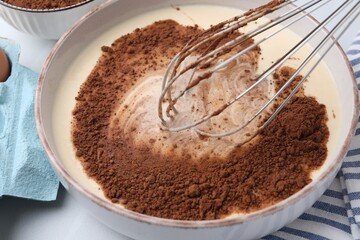 Adding cocoa powder into bowl with dough at white table, closeup