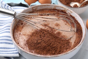 Adding cocoa powder into bowl with dough at white tiled table, closeup