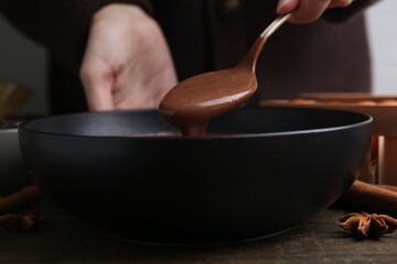 Woman mixing liquid chocolate dough with spoon in bowl at wooden table, closeup