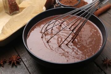 Mixing liquid chocolate dough with whisk in bowl at wooden table, closeup