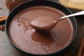 Mixing liquid chocolate dough with spoon in bowl at wooden table, closeup