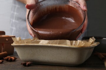 Woman pouring liquid chocolate dough into baking dish at wooden table, closeup