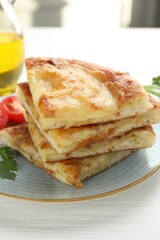 Pieces of delicious Megrelian khachapuri with parsley and tomatoes on white wooden table, closeup