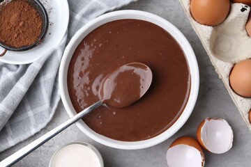 Liquid chocolate dough in bowl and ingredients on grey table, flat lay