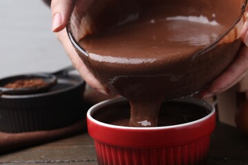 Woman pouring liquid chocolate dough into baking dish at wooden table, closeup
