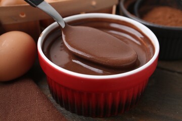 Taking liquid chocolate dough from bowl with spoon on wooden table, closeup