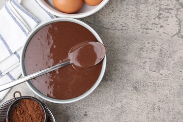 Liquid chocolate dough in bowl and ingredients on grey table, flat lay. Space for text