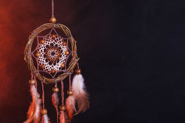 Beautiful dream catcher hanging in color lights on dark background with smoke. Space for text