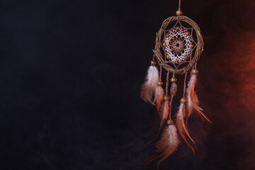 Beautiful dream catcher hanging in color lights on dark background. Space for text