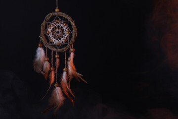 Beautiful dream catcher hanging in color lights on dark background, space for text