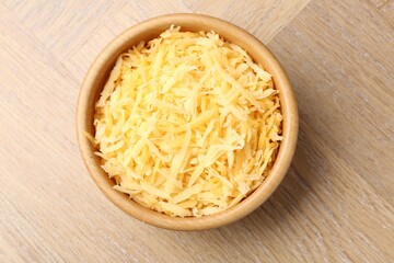 Grated cheese in bowl on wooden table, top view