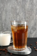Tasty iced coffee, milk and beans on black wooden table