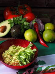 Guacamole in a red bowl, with ingredients at the back. All displayed over a Mexican flag.