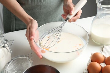 Woman making batter (liquid dough) at white table indoors, closeup