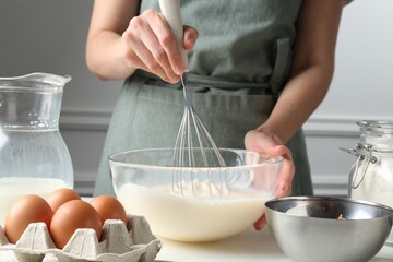 Woman making batter (liquid dough) at white table indoors, closeup