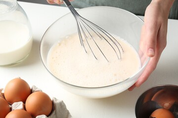 Woman making batter (liquid dough) at white table indoors, closeup