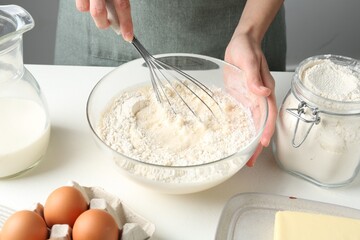 Woman making batter (liquid dough) at white table indoors, closeup