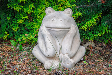 Obraz premium Garden statue of a frog in a thinking pose with green foliage and grass