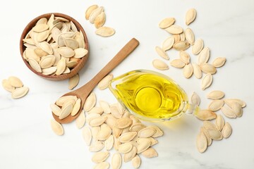 Pumpkin seeds and oil on white table, flat lay