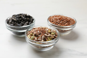 Different seeds in bowls on white table, closeup