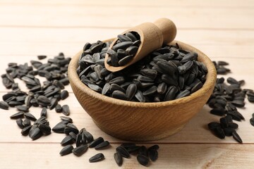 Sunflower seeds and scoop in bowl on white wooden table, closeup