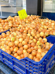 A street market scene with a cart filled with fresh produce. Onions are piled in blue crates