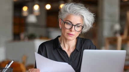 A 40 year old office worker likely an accounting manager or lawyer reviews documents and financial reports on her laptop