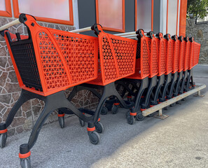 A row of red shopping carts lined up against a wall. The carts are designed for carrying groceries. 