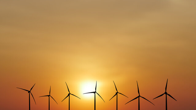 Wind turbines harnessing the power of the sun during a beautiful sunset. They stand tall against the vibrant orange sky, symbolizing sustainable energy.