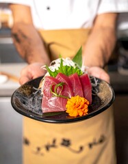 Chef presents plate of fresh sashimi; radish, ginger and garnish