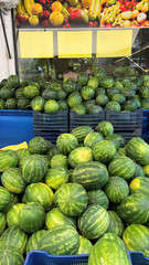A vibrant street market scene with numerous watermelons stacked in blue containers. Fresh fruits 