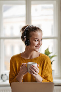 Fototapeta Young female student with headphones sitting at the table and studying.