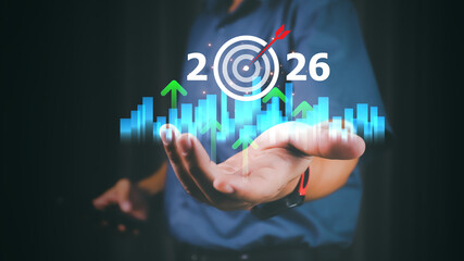 Businessman holding virtual 2026 with rising arrows and target icon, symbolizing new year business goals, strategic vision, future growth, success planning and performance improvement.
