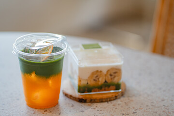 Close up glass of ice yuzu matcha green tea and matcha banoffee on wooden tray of a coffee shop summer terrace, matcha menu photography.